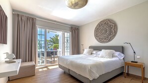 A modern bedroom with a large bed, a desk, and a balcony with a view of palm trees. - Puente Romano Phase 2, Golden Mile, Marbella (Marbella)