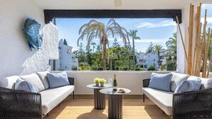 A balcony with two sofas, a small round table, and a bottle of wine. - Puente Romano Phase 2, Golden Mile, Marbella (Marbella)