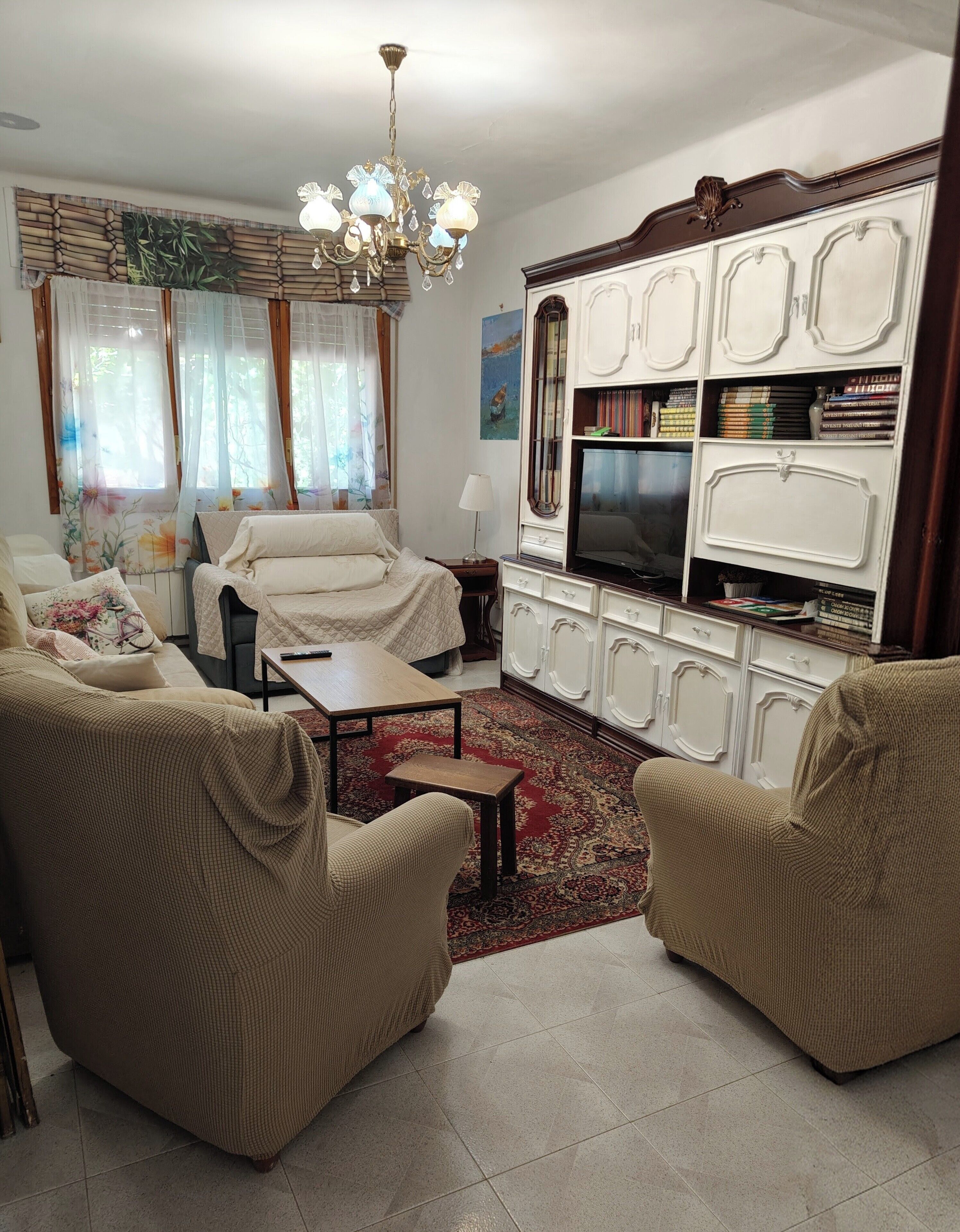 A living room with a sofa set, a TV, a chandelier, and a bookshelf.