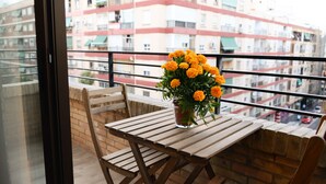 A balcony with a wooden table and chairs, a potted plant with yellow flowers, and a view of multi-story buildings in the background. - Fantastic Apartment in The City of Arts and Sciences (València)