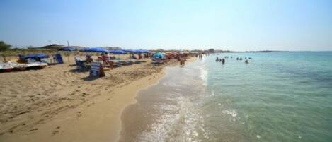 A beach with clear water, umbrellas, and people.