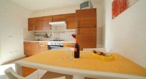 A compact kitchen with wooden cabinets, a dining table, and a wine bottle.