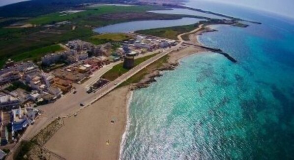 An aerial view of a coastal area with a beach, a pier, and buildings along the shore.