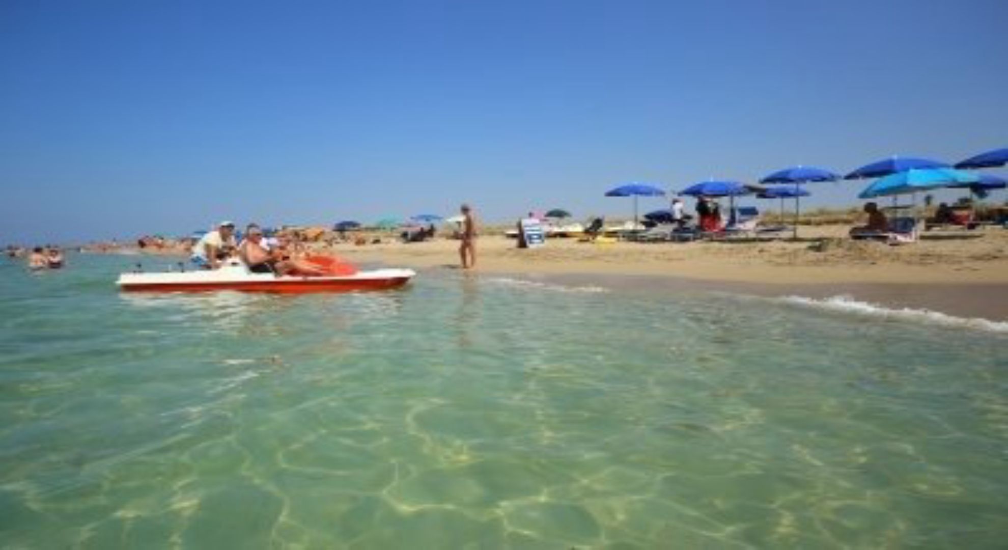Una spiaggia con acque cristalline, una barca e persone sulla riva.