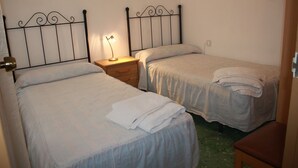 Een kamer met twee eenpersoonsbedden, elk met een nachtkastje en een lamp.