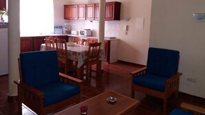 A dining area with a table and chairs, a kitchen in the background, and a blue sofa. - Chã de Arroz Country House (Ribeira Grande)