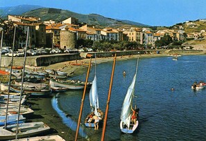 A coastal town with boats docked along the shore, a sandy beach, and buildings in the background. - House with character of  a fisherman (Collioure)