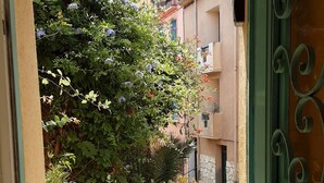 An open doorway leading to a courtyard with a yellow wall, a potted plant, and a tree with blue flowers. - House with character of  a fisherman (Collioure)