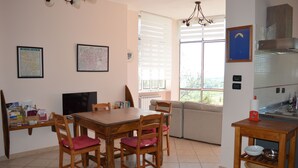 A dining area with a wooden table and chairs, a television, and a window with blinds.