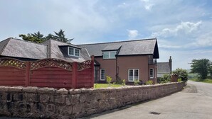 A two-story house with a stone wall in front, a driveway, and a clear sky. - The West Wing, your self contained luxurious rural haven. (Cammachmore)