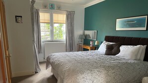 A bedroom with a large bed, a window with curtains, a bedside table with a lamp, and a framed picture on the wall. - The West Wing, your self contained luxurious rural haven. (Cammachmore)