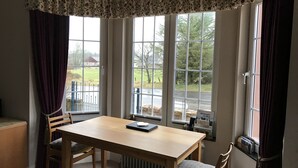A corner room with a wooden table, two chairs, a radiator, and large windows with curtains. - The West Wing, your self contained luxurious rural haven. (Cammachmore)