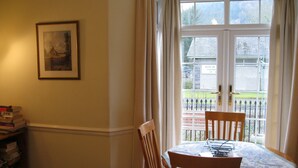 Un comedor con mesa y sillas, una estantería llena de libros, un cuadro en la pared y vistas a un museo a través de una ventana.