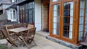 Un patio con una mesa y sillas de madera, un muro de ladrillo y una puerta grande de madera con paneles de vidrio.