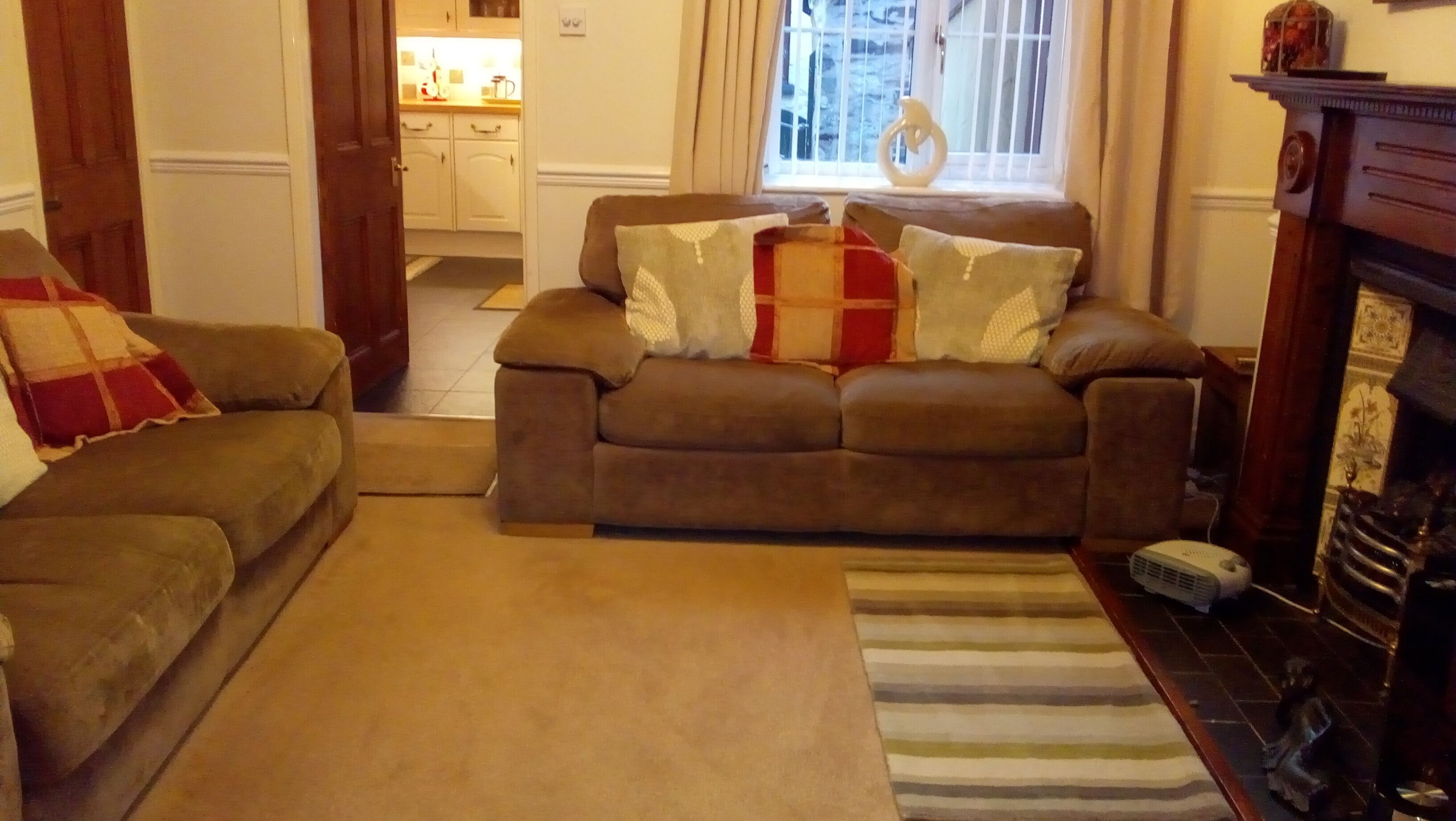 A cozy living room with a brown sofa set, a striped rug, and a fireplace.