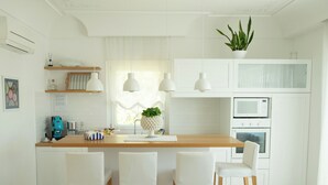 A modern kitchen with white cabinetry, a wooden countertop, and three white chairs.