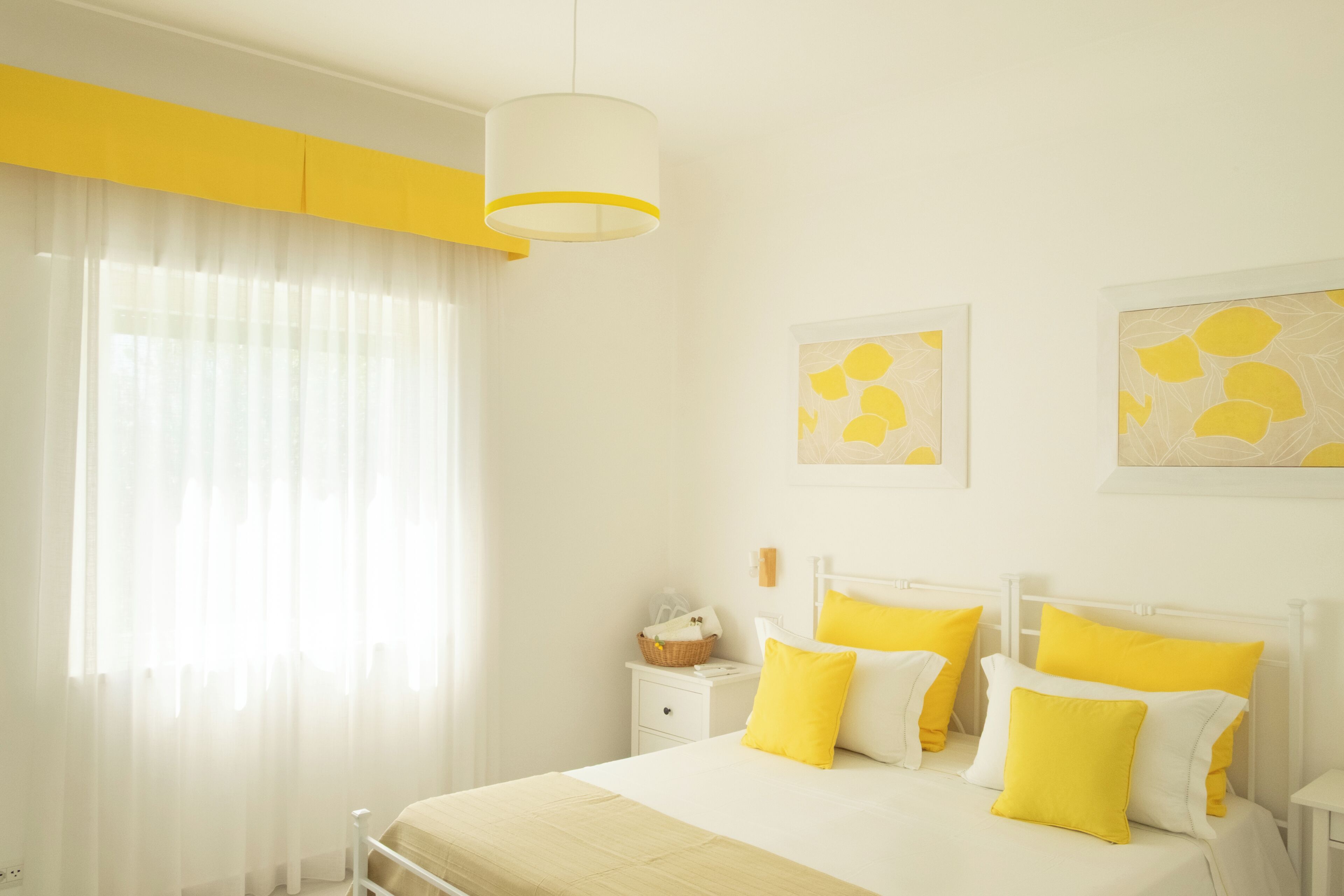 Un dormitorio con cama, mesita de noche blanca y ventana con cortinas translúcidas.