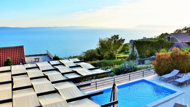 A rooftop pool with a view of the sea, surrounded by greenery and a red-roofed building. - Villa Vedran - A Peaceful Retreat with Stunning Sea Views in Podgora (Podgora)