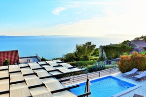 Ein Dachpool mit Blick auf das Meer, umgeben von Grünpflanzen und einem Gebäude mit rotem Dach.