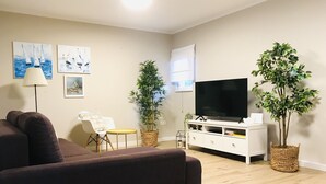 A living room with a sofa, a TV on a white cabinet, two potted plants, a lamp, and artwork on the wall. - Villa Vedran - A Peaceful Retreat with Stunning Sea Views in Podgora (Podgora)