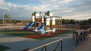 A playground with slides and climbing structures, surrounded by a paved area with benches and a fence. - Villa with Private Pool and Large Underbuild (Gran Alacant)