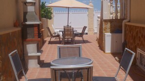 An outdoor patio with a round table and four chairs, a barbecue grill, and a large umbrella providing shade. - Villa with Private Pool and Large Underbuild (Gran Alacant)