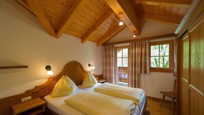 Una habitación con techo de madera, una cama con dos almohadas, una mesita de noche, una silla y una ventana con cortinas.