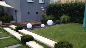 Un espace extérieur moderne doté d’une terrasse en bois, d’escaliers en béton et de jardinières sphériques blanches.