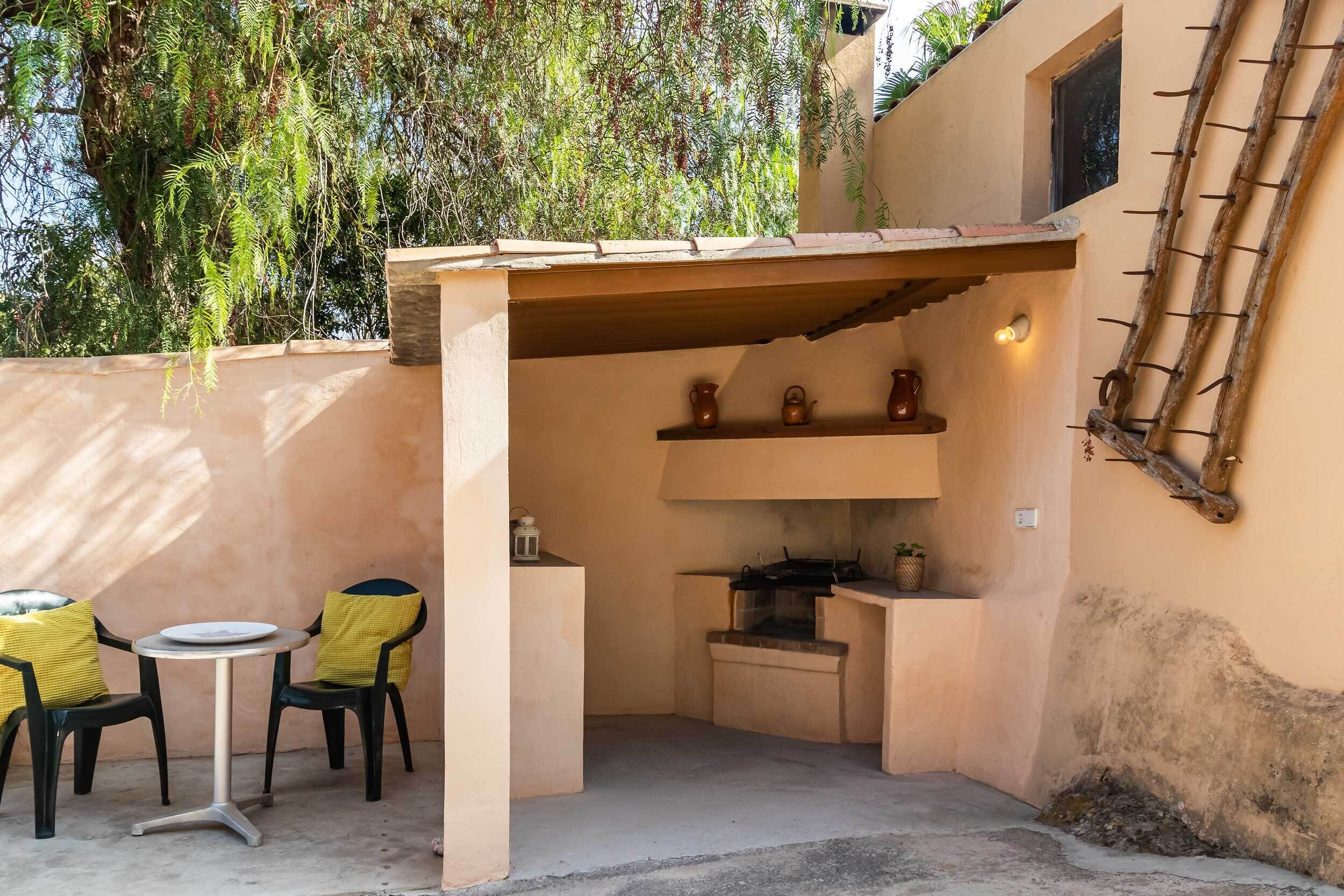 A corner patio with a table and chairs, a shelf with pottery, and a wall-mounted ladder.