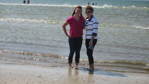 Twee mensen staan op een zandstrand, met de oceaan op de achtergrond.