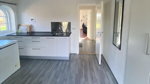 Een moderne keuken met witte kastjes, een zwart aanrecht en een inbouwoven. Links is een raam en er is een deur naar een andere kamer.