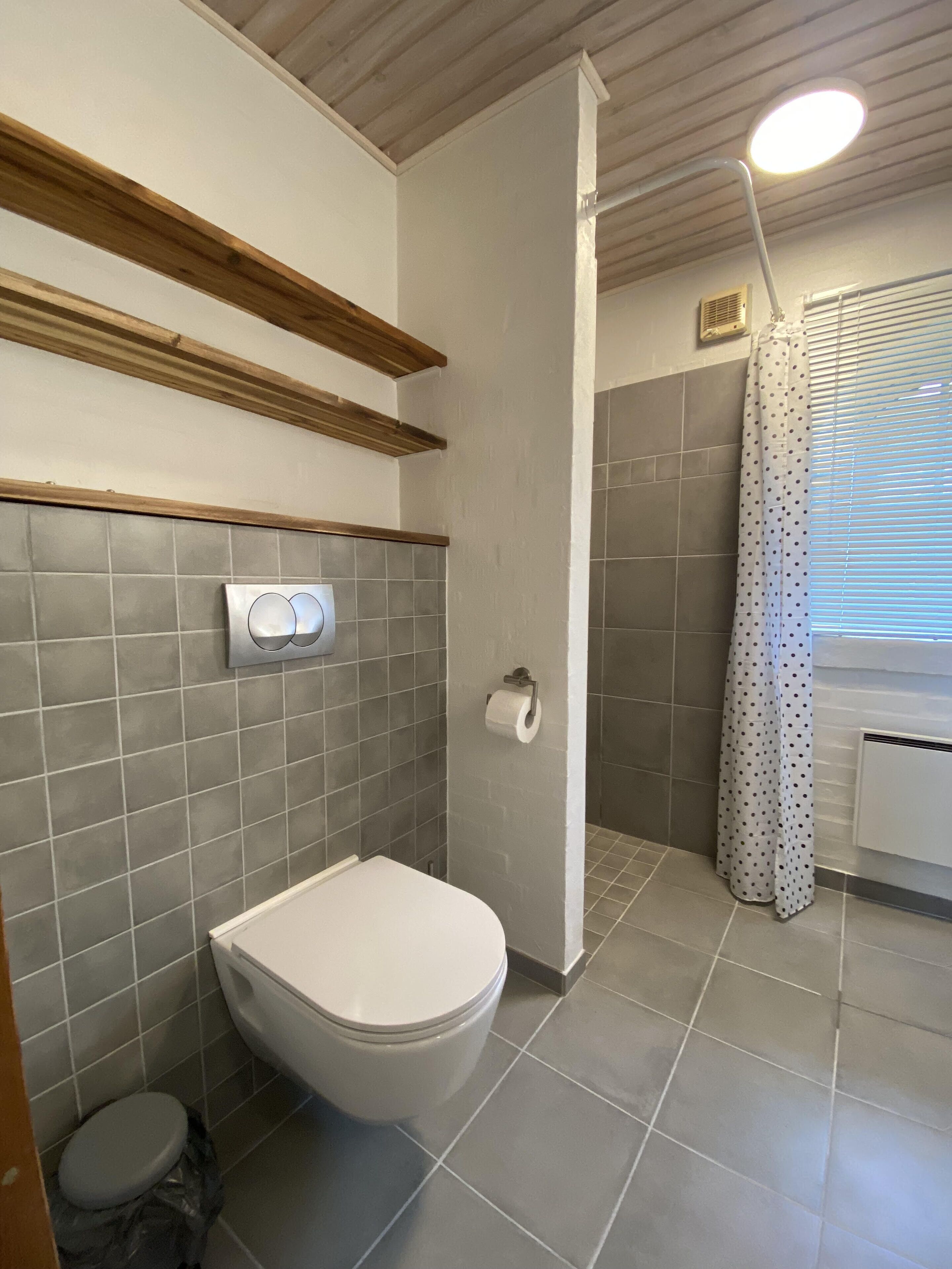 Un baño con inodoro, ducha con cortina y ventana con persianas.