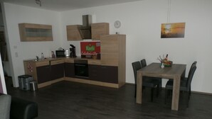 A modern kitchen with a microwave, stove, and wooden cabinets. There is a dining table with chairs and a clock on the wall. - Comfortable child-friendly holiday apartment, Baltic Sea, Usedom, beach, fishing (Peenemünde)
