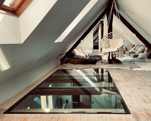Un dormitorio tipo loft con tragaluces, una hamaca y una zona de estar acogedora con cojines y mantas.