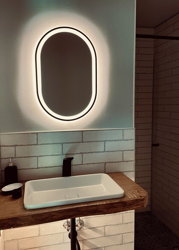 A bathroom with a white sink, a mirror with a light, and a wooden countertop.