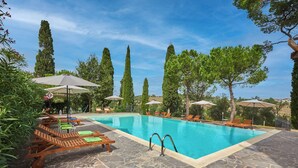 A swimming pool with lounge chairs and umbrellas, surrounded by trees and stone flooring. - Apartment in Torrita, ground floor, terrace with view, swimming pool, 4 people (Torrita di Siena)