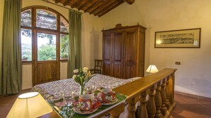 A room with a wooden bed, a dining table set with tea cups and saucers, a wooden cabinet, and a large window with curtains. - Apartment in Torrita, ground floor, terrace with view, swimming pool, 4 people (Torrita di Siena)