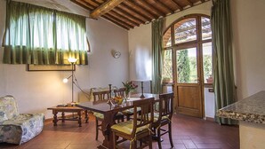 A dining area with a wooden table and chairs, a lamp, and a view through a window with curtains. - Apartment in Torrita, ground floor, terrace with view, swimming pool, 4 people (Torrita di Siena)