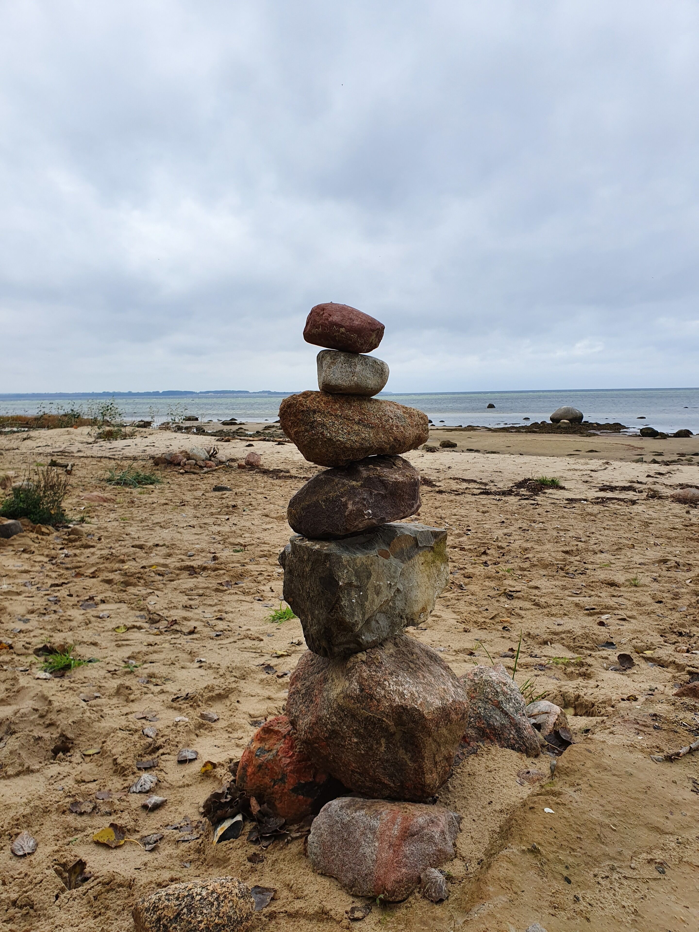 A stack of rocks on a sandy beach with a view of the ocean and overcast sky.