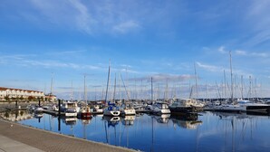 Un port de plaisance où sont amarrés de nombreux voiliers, une surface d’eau calme qui reflète les bateaux et un ciel bleu dégagé.