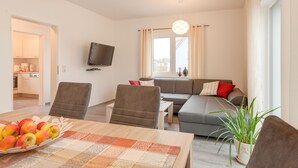 A modern living room with a sofa, chairs, a TV, and a dining area with fruit. - Holiday home on the Baltic Sea - up to 6 persons (4 stars) (Zierow)