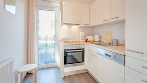 A modern kitchen with white cabinets, a built-in oven, a coffee maker, and a small dining table. - Holiday home on the Baltic Sea - up to 6 persons (4 stars) (Zierow)