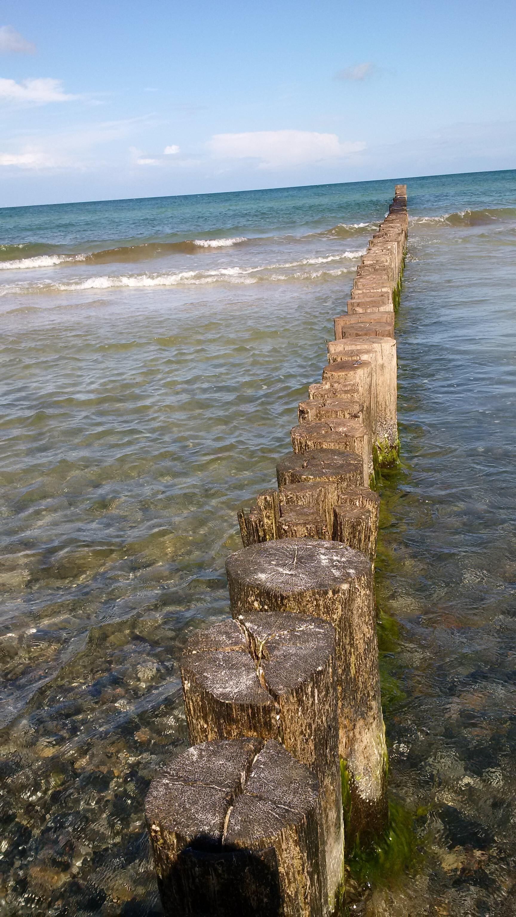 Een lange, verweerde houten pier die zich uitstrekt over rustig water, met heldere lucht erboven.