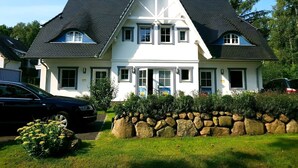 Ein zweigeschossiges Haus mit einem steilen Satteldach, vielen Fenstern und einer Steinwand davor.