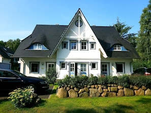 Une maison à deux étages, dotée d’un toit à forte pente, de nombreuses fenêtres et d’un mur de pierre à l’avant.