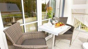 Ein Balkon mit Korbstühlen, einem Tisch mit weißer Tischdecke, einer Blumenvase und einem Obstkorb.