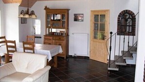 Una stanza accogliente con soffitto in legno, un tavolo da pranzo con sedie, un divano, un armadio e una scala con ringhiera in legno.