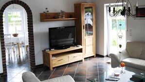 Un soggiorno con televisore su un mobile in legno, un divano, un tavolino da caffè e un'area pranzo con tavolo e sedie.