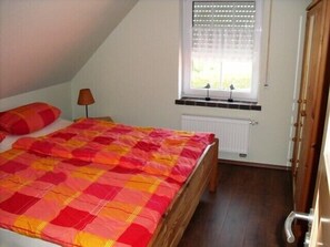 A bedroom with a bed, a window with blinds, a radiator, and a wooden door.