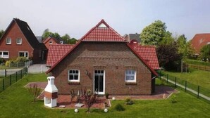 Una casa a due piani con tetto rosso, facciata in mattoni e un piccolo giardino anteriore con una struttura decorativa bianca.